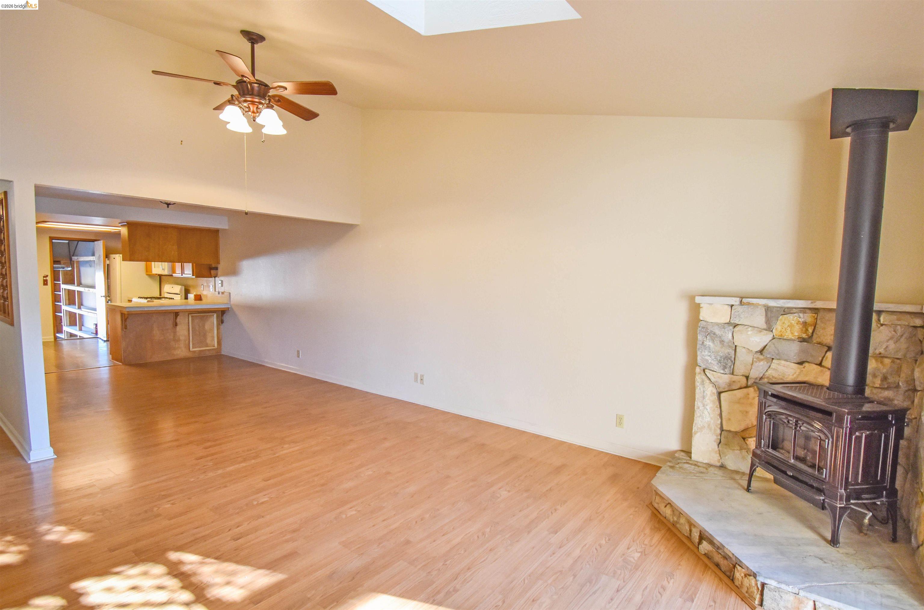 23685 Marble Quarry Road, Unit 22 Columbia, CA 95310 - Photo 5 of 33 Unfurnished living room with ceiling fan, vaulted ceiling, a wood stove, light wood finished floors, and a skylight