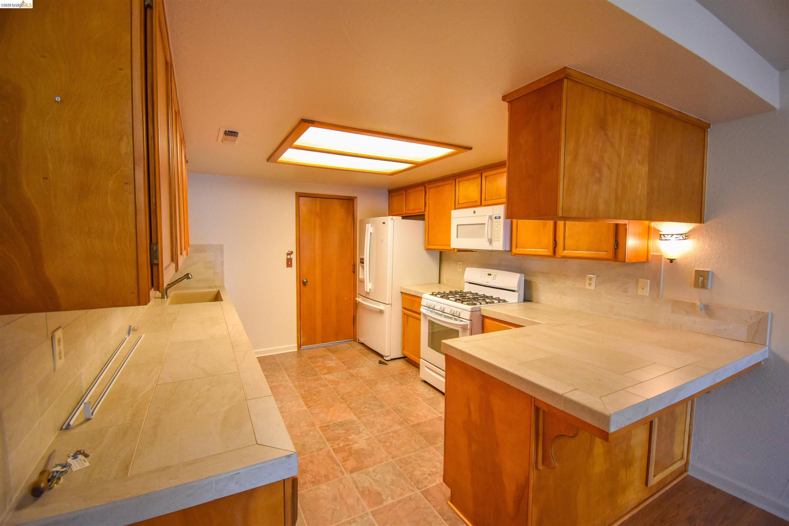 23685 Marble Quarry Road, Unit 22 Columbia, CA 95310 - Photo 9 of 33 Kitchen with white appliances, tile counters, a peninsula, backsplash, and wood finish cabinetry