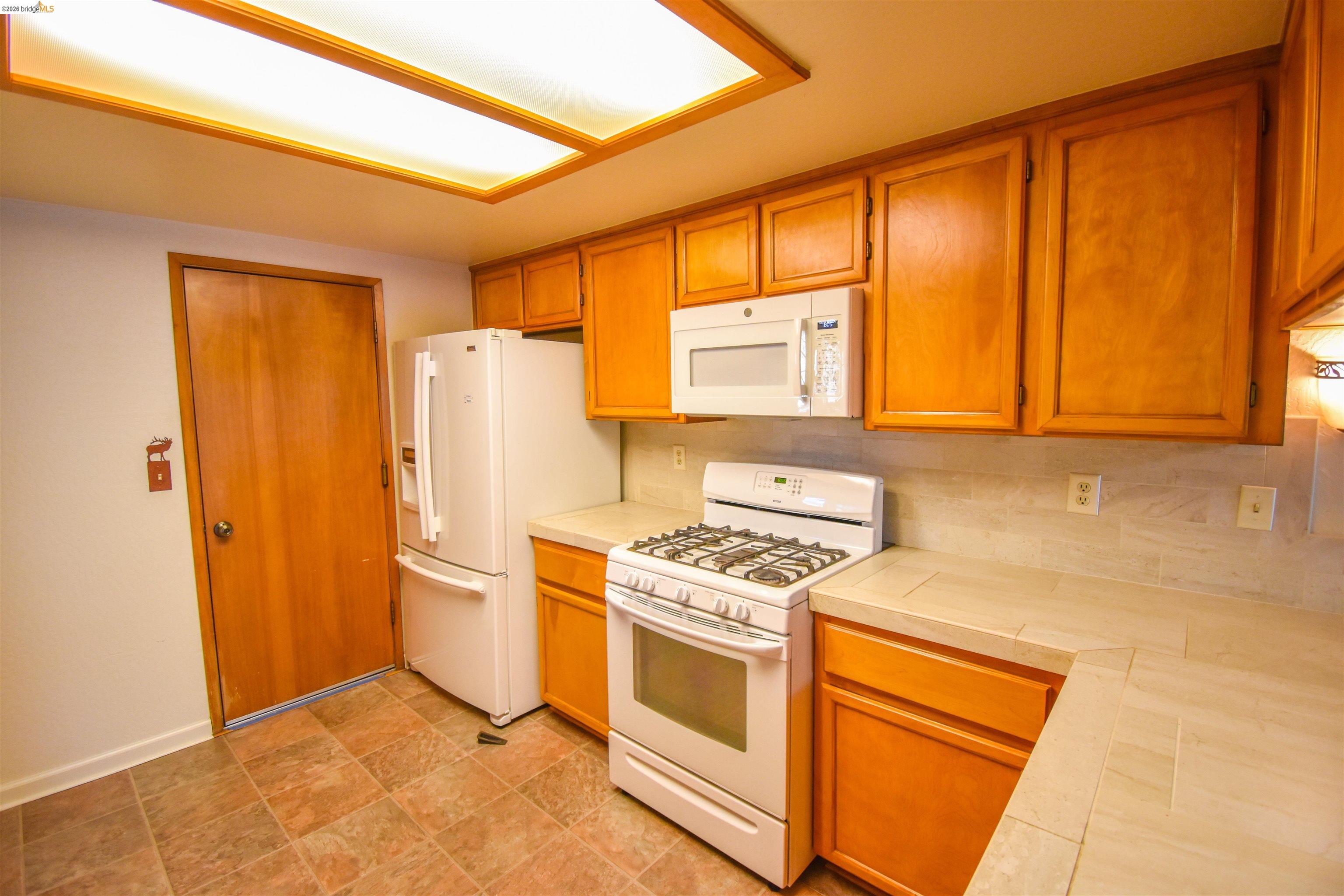 23685 Marble Quarry Road, Unit 22 Columbia, CA 95310 - Photo 10 of 33 Kitchen with white appliances, tile countertops, wood finish cabinetry, and stone finish flooring
