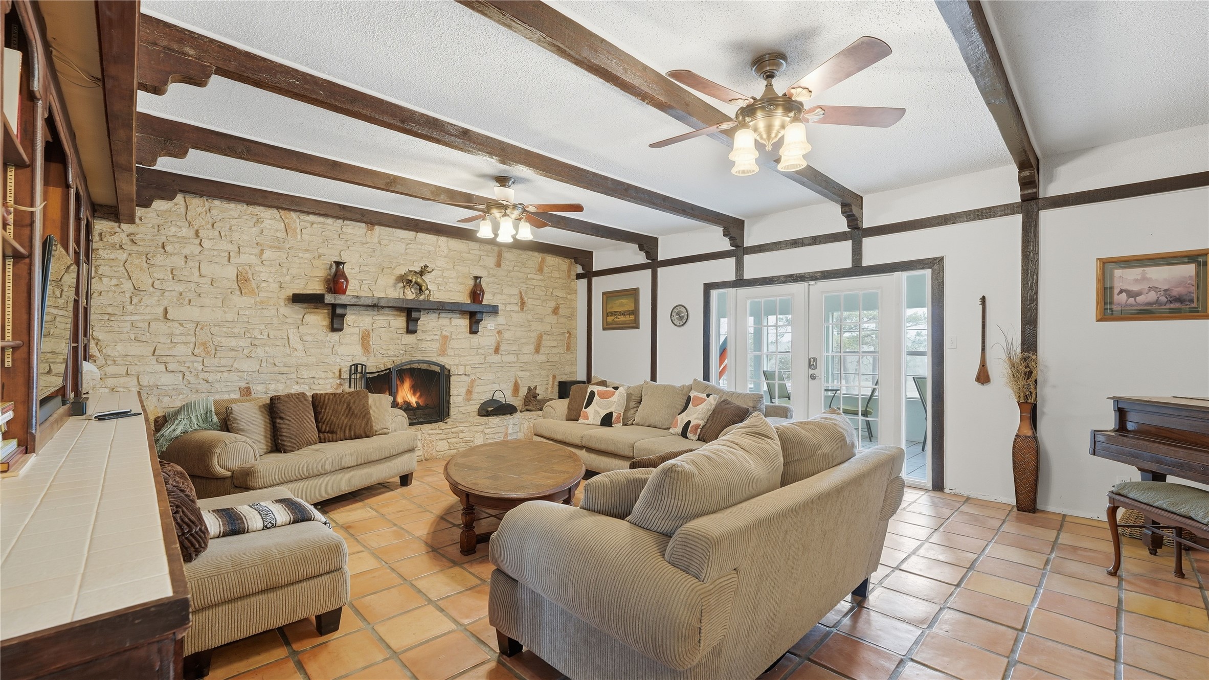 182 Little Ranch Road Red Rock, TX 78662 - Photo 31 of 40 Tiled living area with french doors, a textured ceiling, a stone fireplace, beam ceiling, and ceiling fan