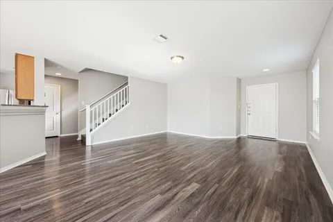 a view of an empty room with wooden floor and stairs