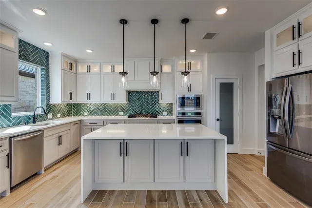 a large kitchen with stainless steel appliances kitchen island granite countertop a refrigerator a oven and white cabinets with wooden floor