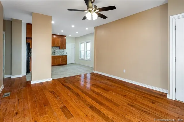 a view of an empty room with wooden floor and a ceiling fan
