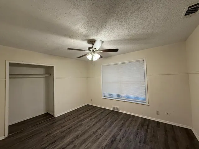 an empty room with wooden floor fan and windows