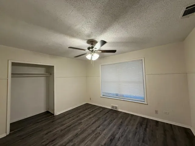 an empty room with wooden floor fan and windows