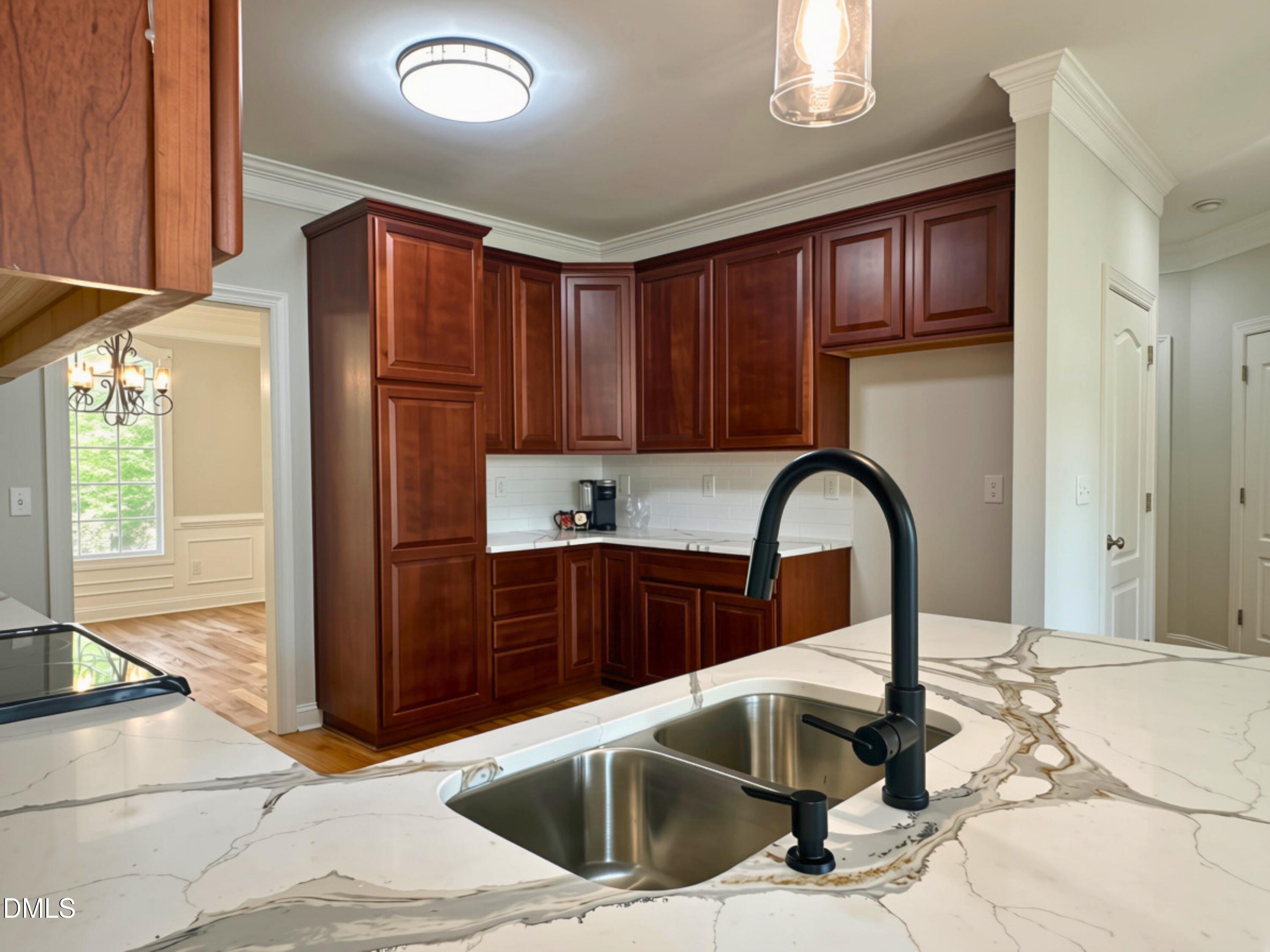 3100 Donlin Drive Wake Forest, NC 27587 - Photo 16 of 67 Kitchen featuring light-toned countertops with dark veining, a double stainless steel sink with a matte black faucet, wood-finish cabinetry, and a white subway tile backsplash