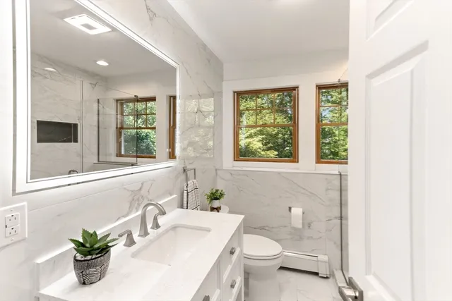 a bathroom with a granite countertop toilet a sink a large mirror and a window