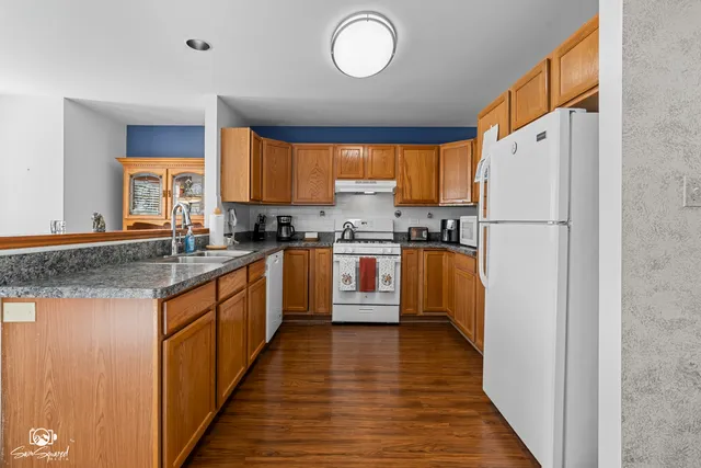 a kitchen with granite countertop a refrigerator a sink dishwasher a stove with wooden cabinets and floor