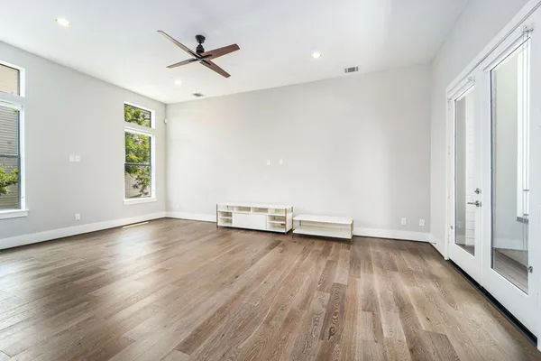an empty room with wooden floor chandelier fan and windows