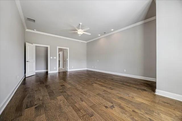 a view of an empty room with wooden floor and a ceiling fan
