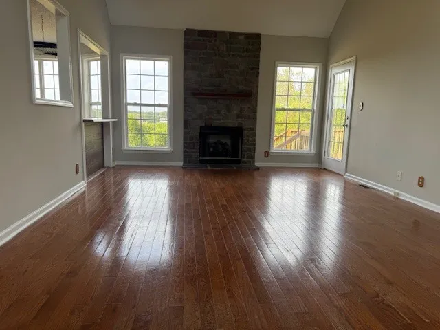 an empty room with wooden floor fireplace and windows