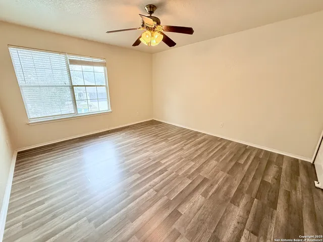 an empty room with wooden floor fan and windows