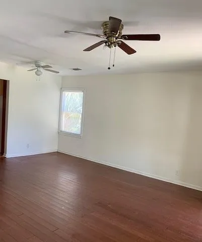 an empty room with wooden floor ceiling fan and windows