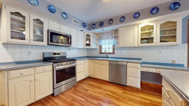 a kitchen with stainless steel appliances granite countertop a refrigerator a oven and white cabinets with wooden floors