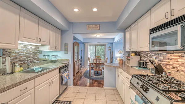 a kitchen with stainless steel appliances granite countertop a stove a sink dishwasher and white cabinets with wooden floor
