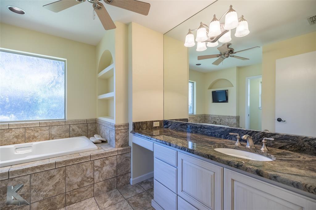 220 Hedges Road Abilene, TX 79605 - Photo 22 of 40 a bathroom with a granite countertop sink a large mirror and a bathtub with shower