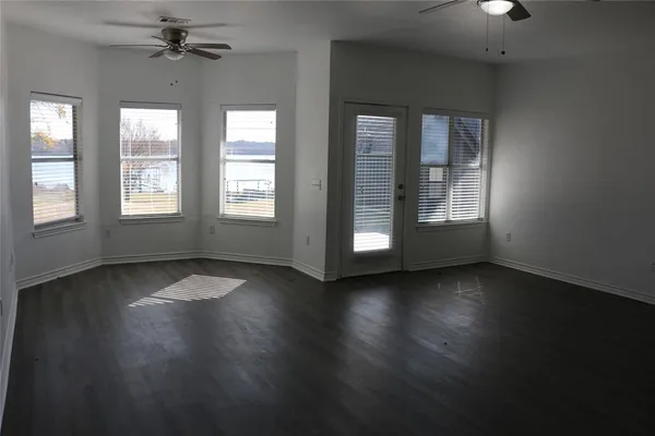 an empty room with wooden floor chandelier fan and windows