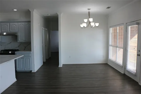 a view of an empty room with wooden floor and a kitchen