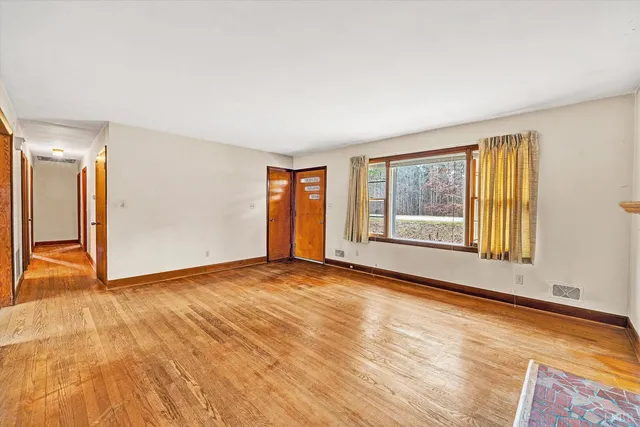 a view of an empty room with wooden floor and a window