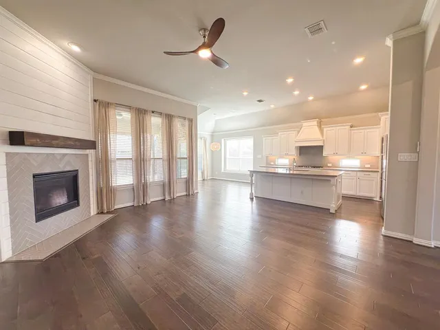 a view of an empty room with wooden floor and a kitchen
