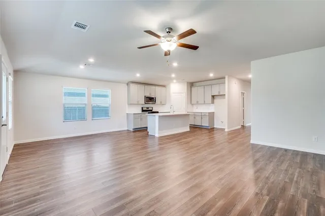 a view of an empty room with wooden floor and a kitchen