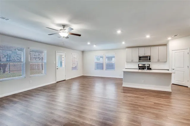 a view of an empty room with wooden floor and a ceiling fan