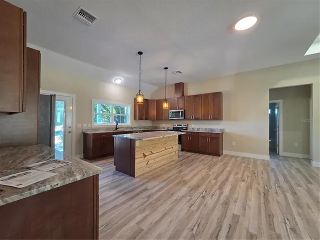 a kitchen with stainless steel appliances granite countertop wooden cabinets a stove a sink and a wooden floors