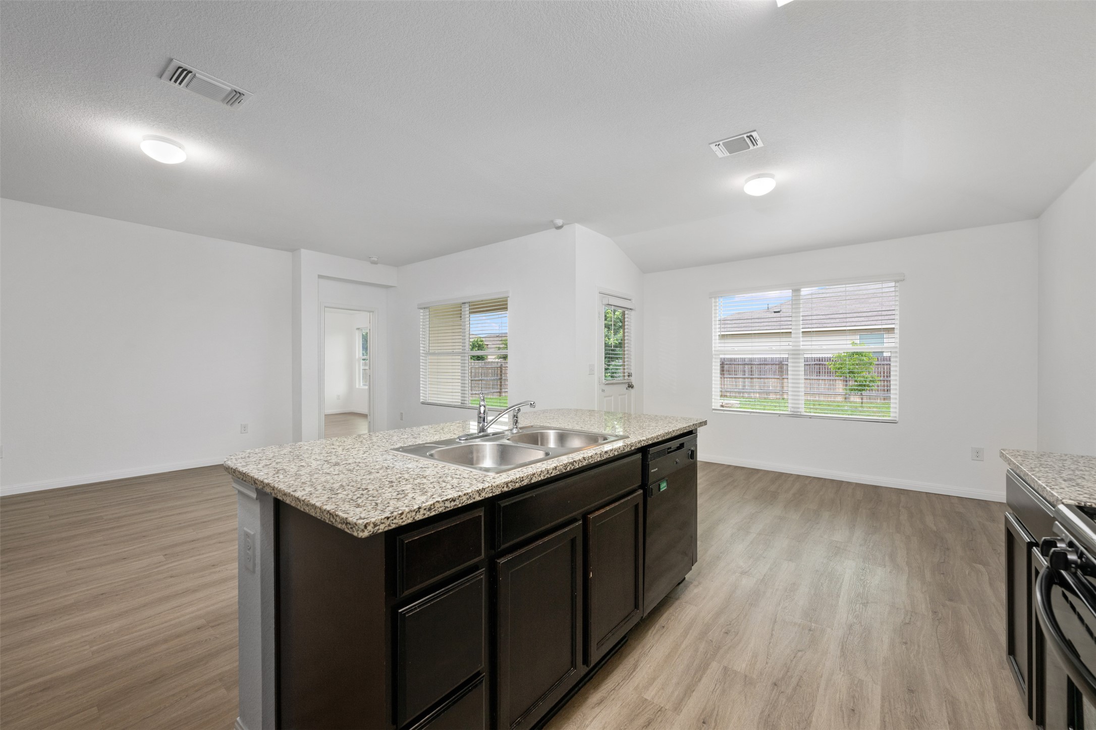 14900 Retha Pass Austin, TX 78725 - Photo 13 of 39 Kitchen island featuring a dual basin sink, integrated dishwasher, and a light-toned granite countertop