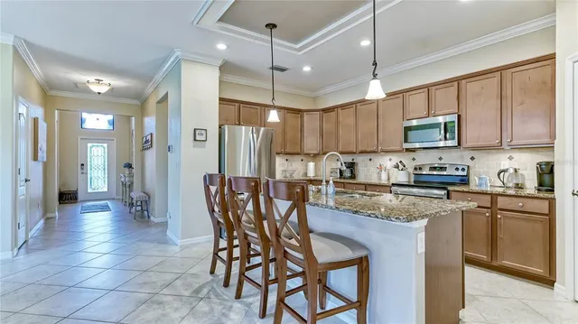 a kitchen with stainless steel appliances granite countertop wooden cabinets a refrigerator a sink a stove a dining table and chairs