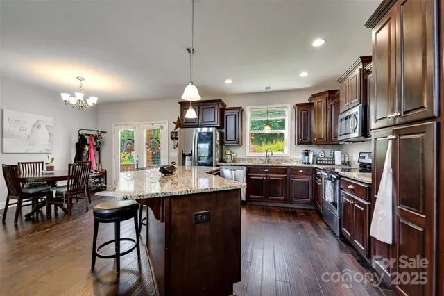 a kitchen with stainless steel appliances granite countertop a stove a refrigerator a dining table and chairs with wooden floor