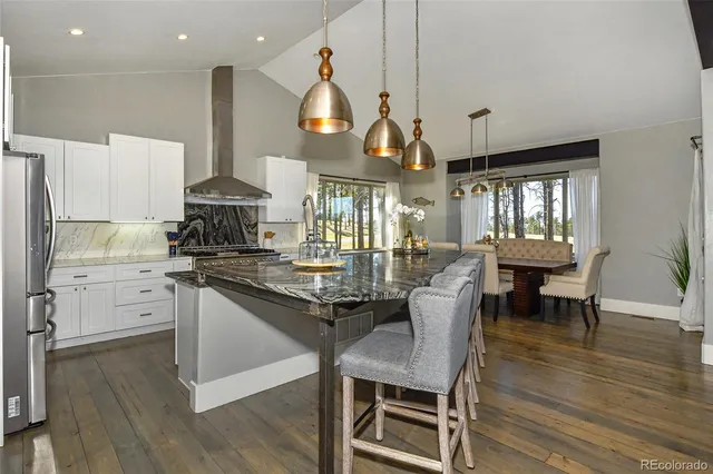 a kitchen with stainless steel appliances kitchen island granite countertop a stove a refrigerator a dining table and chairs with wooden floor