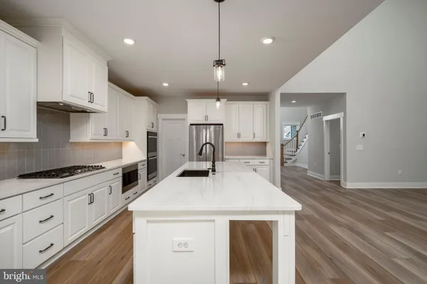 a kitchen with granite countertop a stove a sink a refrigerator and white cabinets with wooden floor
