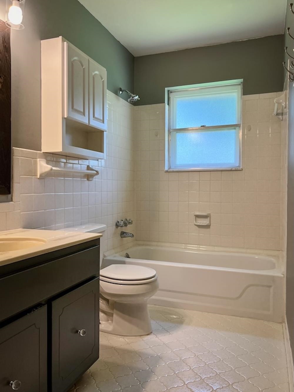 7935 Memphis Arlington Road Bartlett, TN 38133 - Photo 11 of 20 Bathroom featuring a white subway tile surround, a built-in bathtub, a window, a dark vanity with a light-colored countertop, and patterned floor tiles