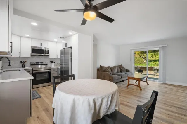 a kitchen with stainless steel appliances kitchen island granite countertop a refrigerator a stove a sink a dining table and chairs with wooden floor