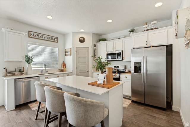 7693 West Mount Elinor Road Magna, UT 84044 - Photo 8 of 33 Kitchen featuring white shaker cabinetry, stainless steel appliances, a center island with countertop seating, and wood-finish flooring