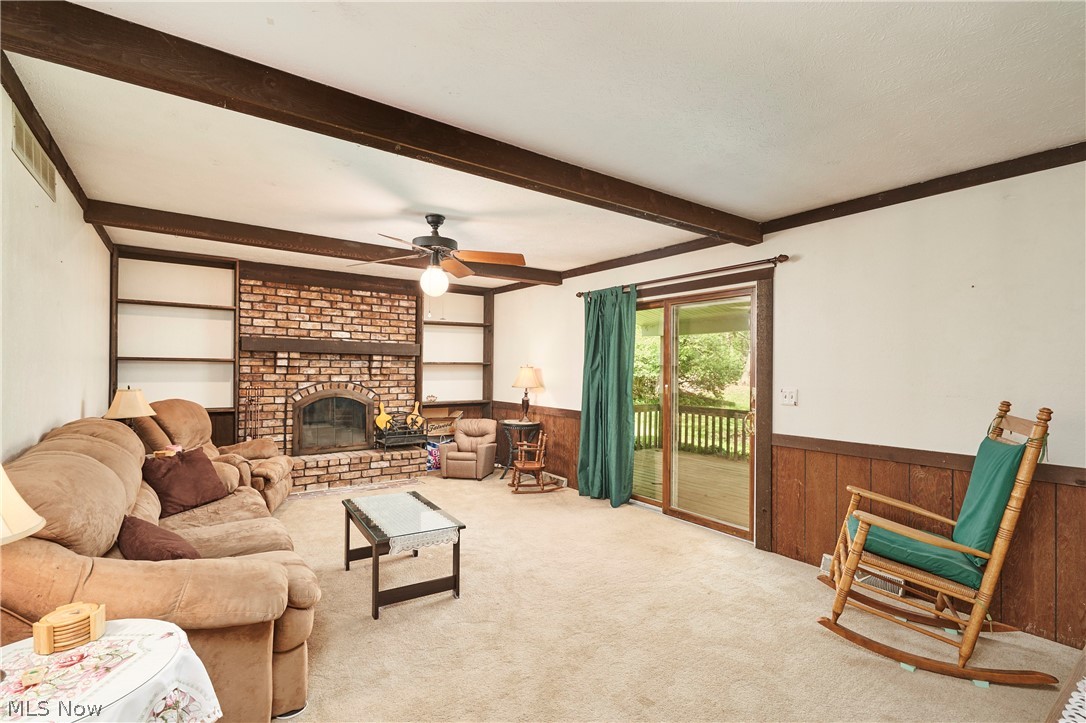 3097 Baughman Road Clinton, OH 44216 - Photo 4 of 27 Living area featuring a floor-to-ceiling brick fireplace with an arched firebox, built-in shelving, exposed ceiling beams, and sliding glass doors opening to a wood deck