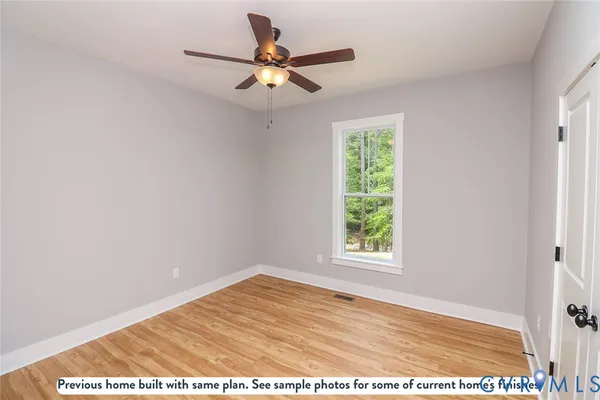 a view of an empty room with wooden floor and a ceiling fan