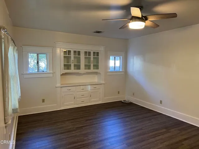 an empty room with wooden floor chandelier fan and windows
