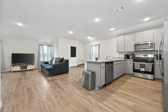 a large living room with stainless steel appliances granite countertop a stove top oven a sink dishwasher and a refrigerator with wooden floor