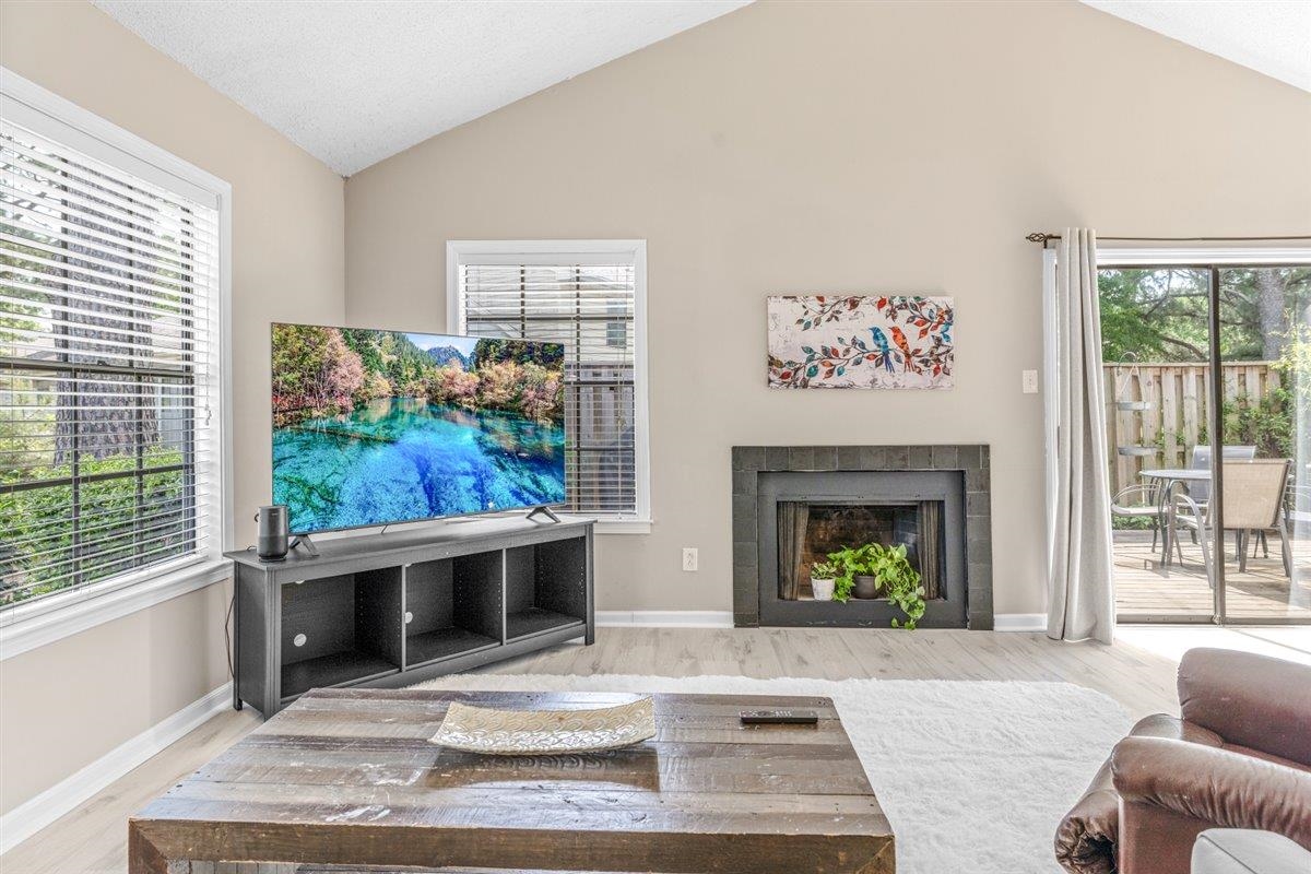 2976 Kin Cove, Unit 2976 Memphis, TN 38119 - Photo 5 of 24 Living area featuring vaulted ceilings, wood-finish flooring, a dark-tiled fireplace, and sliding glass doors opening to an outdoor patio