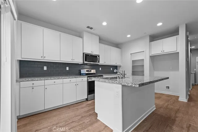 a kitchen with stainless steel appliances kitchen island granite countertop a stove top oven a sink a refrigerator and white cabinets