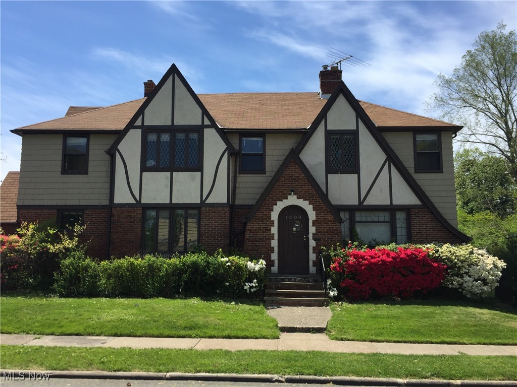 Tudor house featuring brick siding, stucco siding, a chimney, and a front yard