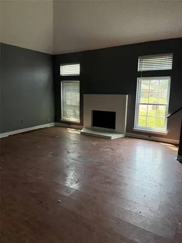 an empty room with wooden floor fireplace and windows