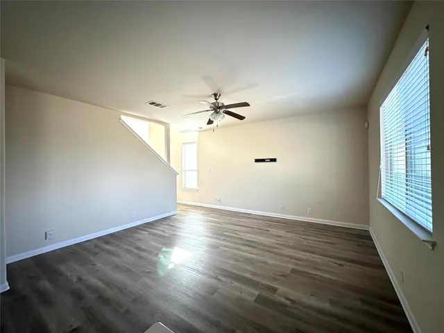 an empty room with wooden floor fan and windows