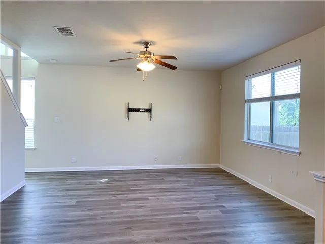 an empty room with wooden floor fan and windows