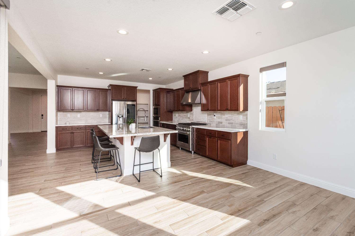 124 Basile Court Lincoln, CA 95648 - Photo 11 of 55 kitchen featuring a kitchen breakfast bar, light wood-style flooring, stainless steel appliances, a kitchen island with sink, and light stone counters