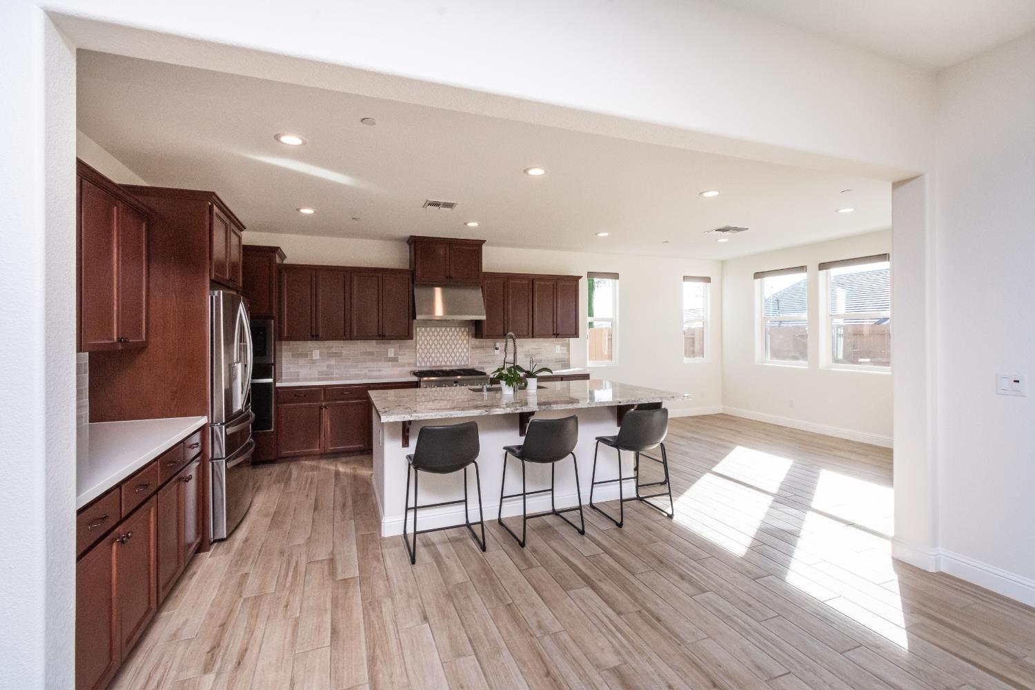 124 Basile Court Lincoln, CA 95648 - Photo 9 of 55 kitchen featuring a kitchen bar, recessed lighting, a center island with sink, light stone countertops, and stainless steel appliances