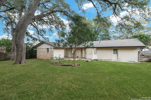 a backyard of a house with table and chairs and a large tree
