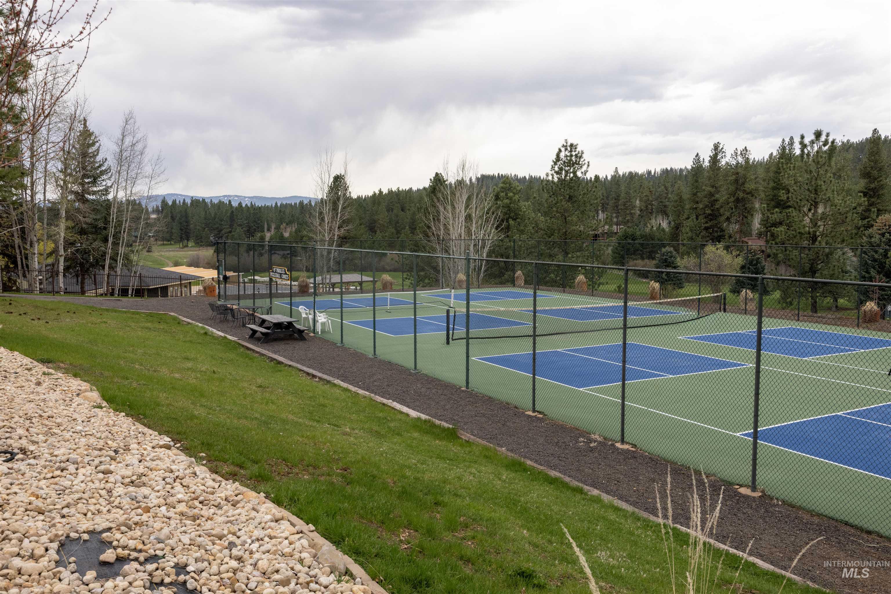 3873 Hot Springs Road New Meadows, ID 83654 - Photo 21 of 25 Multiple fenced pickleball courts featuring green and blue surfacing, bordered by a gravel path