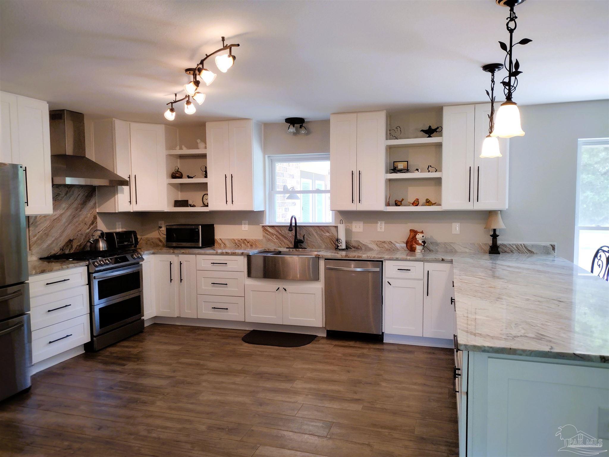 4611 Gunter Road Milton, FL 32570 - Photo 4 of 29 a kitchen with granite countertop a stove top oven a sink dishwasher and white cabinets with wooden floor